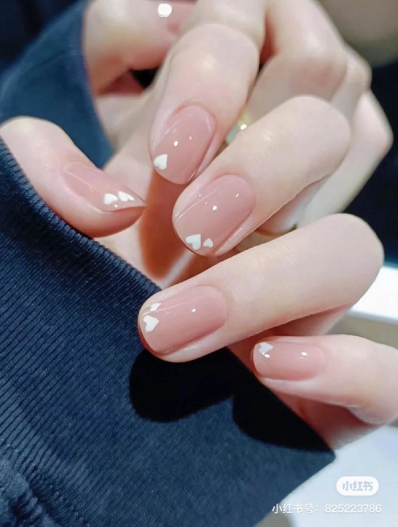 Bàn tay với móng tay sơn màu nude trang trí họa tiết trắng đơn giản, trên nền áo xanh đậm.