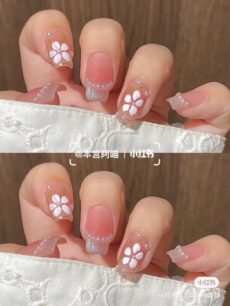 Bộ móng tay được trang trí hoa trắng, ngọc trai và nhũ bạc trên nền màu hồng nhạt.