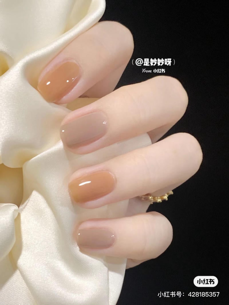 Bàn tay với móng tay sơn màu nâu nhạt, cầm một dải lụa màu trắng, nền đen.