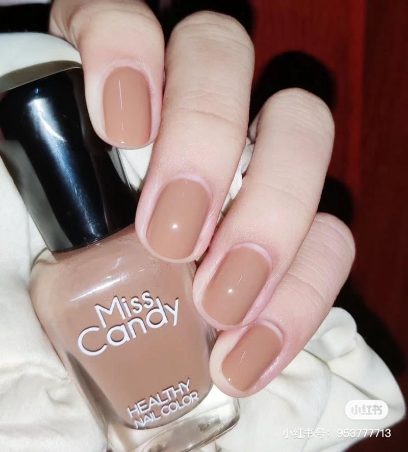 Bàn tay với móng sơn màu nâu bóng, cầm lọ sơn có nhãn "Miss Candy".