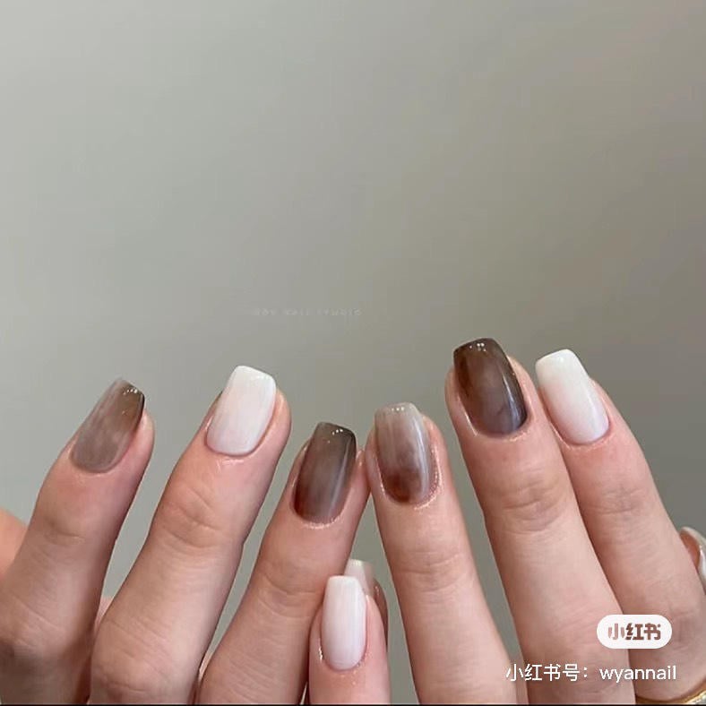 Bàn tay với móng tay sơn màu trắng và nâu, thiết kế ombre, trên nền xám nhạt.