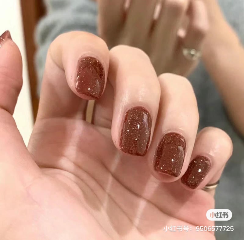 Bàn tay với móng tay sơn màu nâu lấp lánh, được chụp cận cảnh.