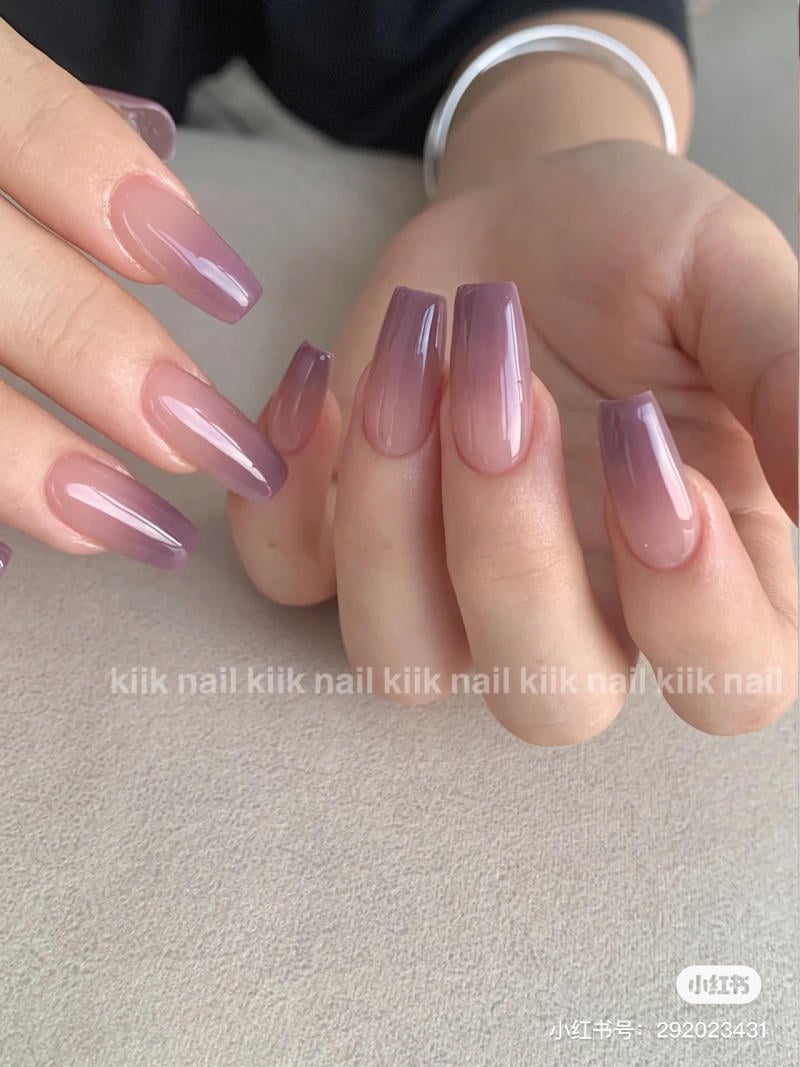 nail-mau-tim__21__36b514ecd0c649d98d3e17a53631030f Bàn tay với móng tay dài được sơn màu tím nhạt bóng loáng, nền xám nhạt.