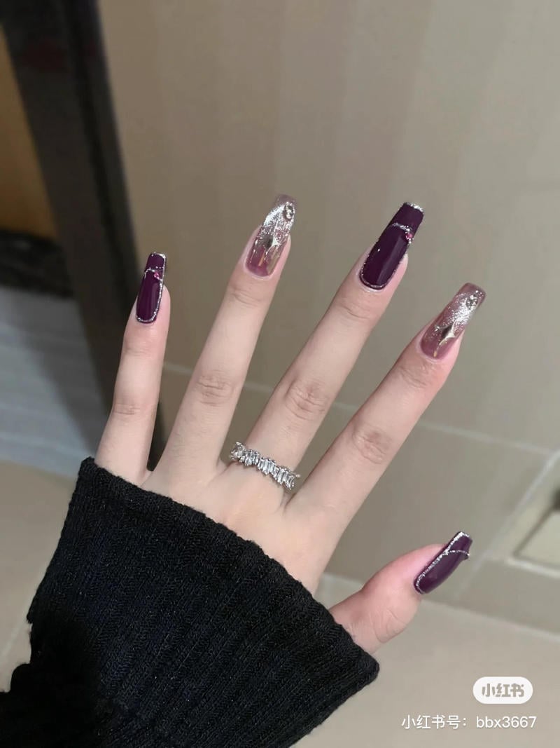 nail-mau-tim__34__d20e8b510c0f4ba398ccbee4befe2e6e Bàn tay với móng được sơn màu tím và ánh kim tuyến, đeo nhẫn bạc, áo len đen.