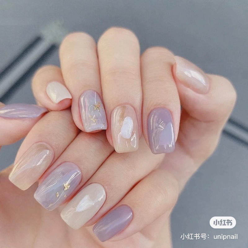 nail-mau-tim__36__101ad814e8fa49ba93dd86b20e676a64 Bàn tay với móng tay được sơn màu pastel và trang trí họa tiết nhẹ nhàng, ánh sáng phản chiếu trên bề mặt móng.