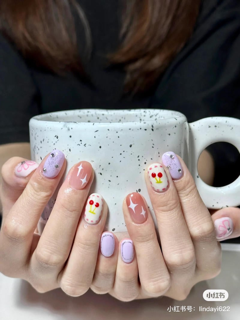 nail-mau-tim__45__4d7328b4c4dc401e8e2a3604f8568a0e Bàn tay với móng tay được trang trí họa tiết nhiều màu sắc, cầm một chiếc cốc màu trắng có đốm đen.