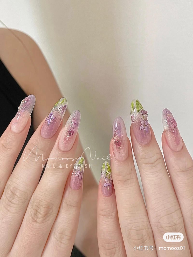 nail-mau-tim__48__1fa00359e9a540edad7c82598a534b8f Bàn tay với móng tay dài được trang trí nghệ thuật với màu hồng và xanh lá, kèm họa tiết lấp lánh.