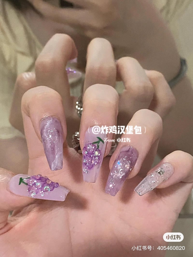 nail-mau-tim__54__945fb52af17248b9afc084746e3e861b Bàn tay với móng tay dài, sơn màu tím nhạt, trang trí hoa và kim tuyến lấp lánh.
