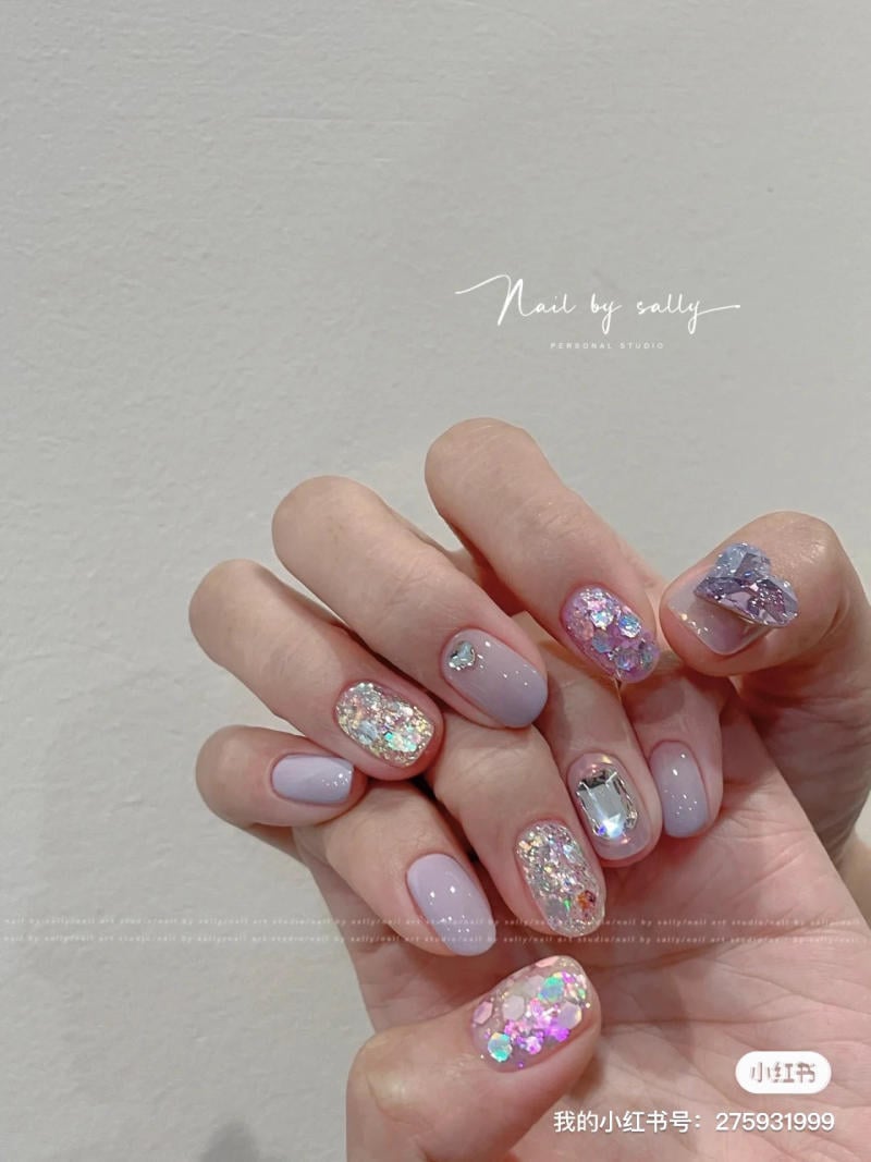 nail-mau-tim__57__160781437d3c48e790d475669a18ad7a Bàn tay với móng tay được trang trí họa tiết lấp lánh và đá quý trên nền màu pastel nhẹ nhàng.