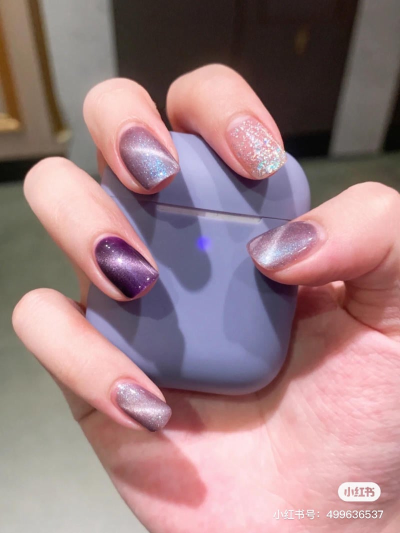 nail-mau-tim__63__fcd757e869c34efab61328186939be0c Bàn tay với móng tay sơn màu tím và bạc lấp lánh, cầm hộp đựng tai nghe màu xám.