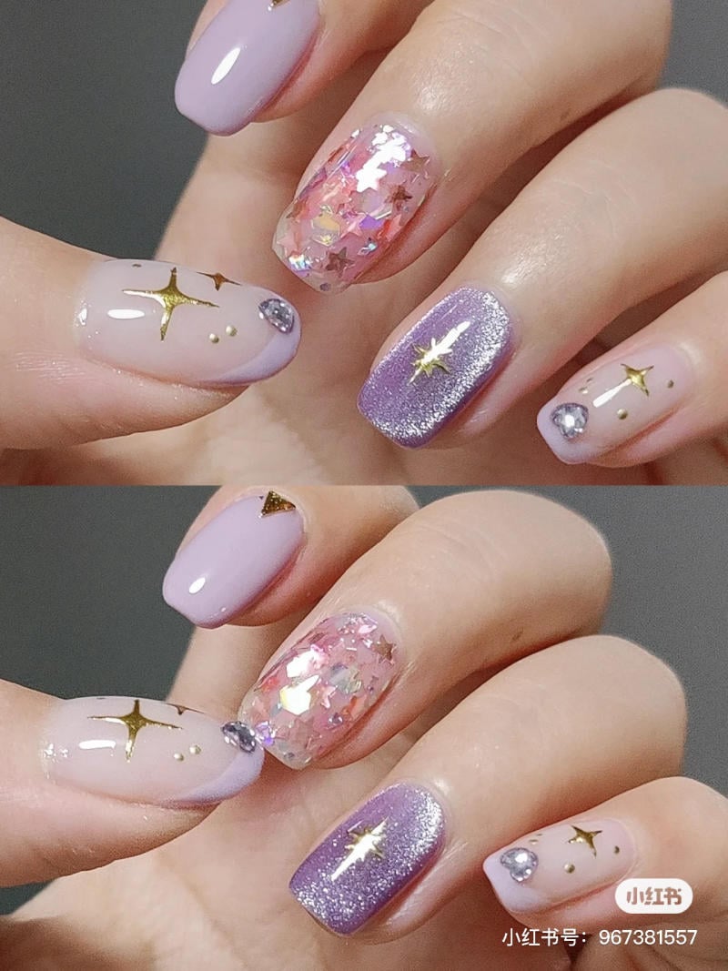 nail-mau-tim__64__fa529c75ebc540eb83a99634ac247c42 Bàn tay với móng tay trang trí họa tiết ngôi sao và kim tuyến màu tím, hồng và ánh vàng lấp lánh.