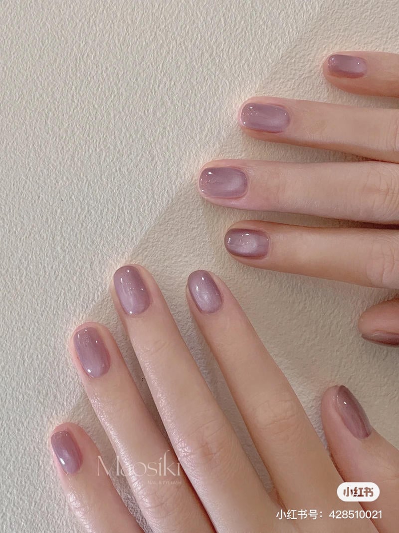 nail-mau-tim__65__eef8c100d42d40a3af77a9577e7150dd Bàn tay với móng tay được sơn màu tím nhạt, trên nền bề mặt có kết cấu nhẵn.