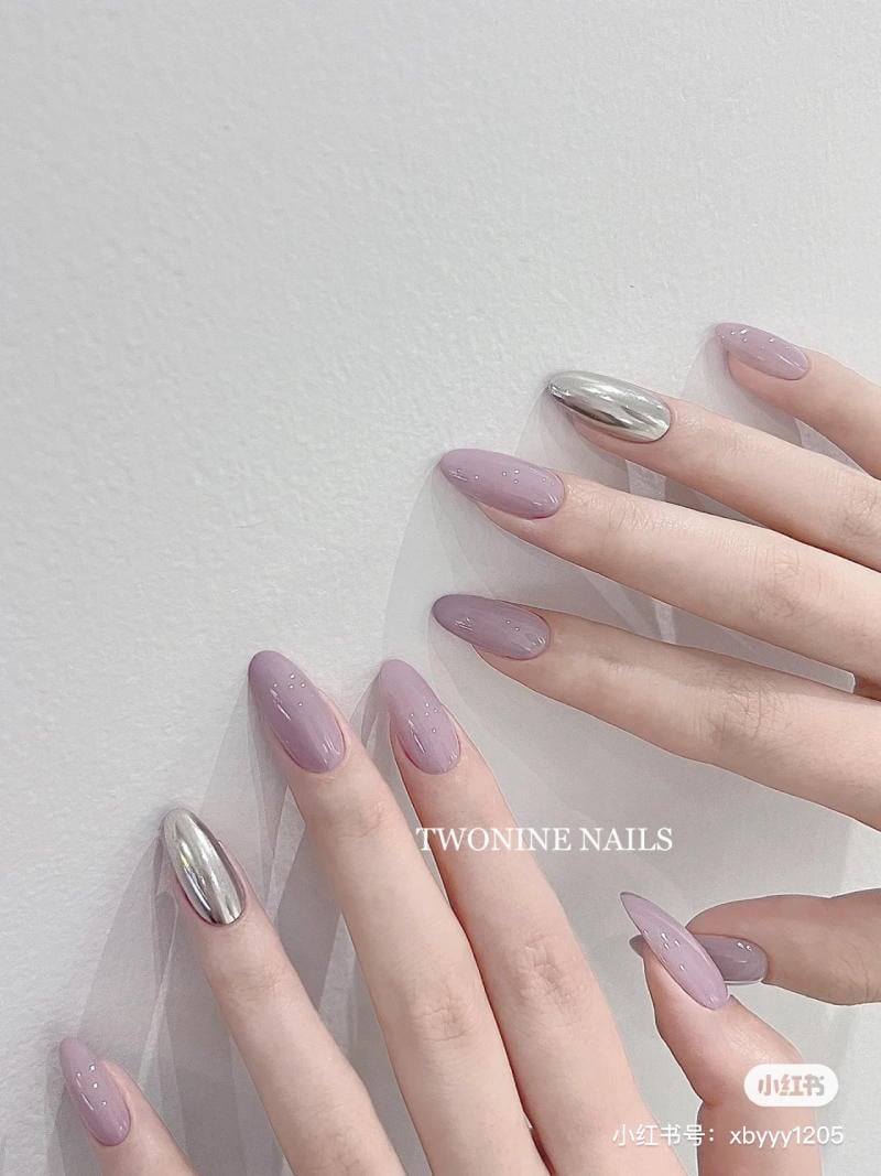 nail-mau-tim__72__92209613422a4b2b8e36725cd6f07d6e Bàn tay với móng tay sơn màu hồng tím và bạc bóng, nền trắng.