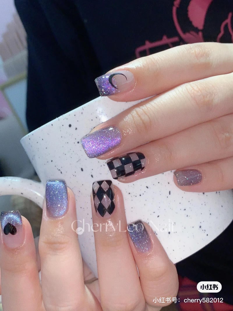 nail-mau-tim__73__5ce568983e3f44a694547057880a8f6c Bàn tay với móng tay được trang trí họa tiết lấp lánh và hình học, cầm một chiếc cốc trắng có chấm đen.