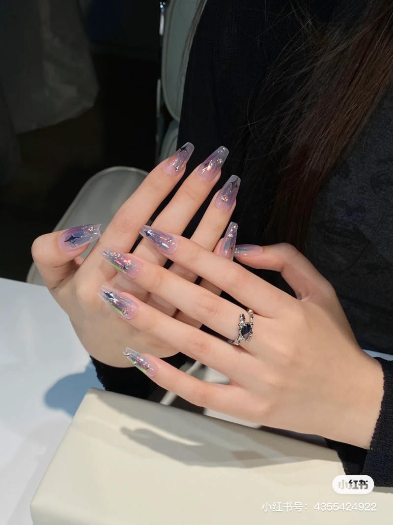 nail-mau-tim__87__1a0d1c127b614b86932a5ef4ced6428e Đôi tay với móng tay dài, được sơn màu ombre tím ánh kim và đeo nhẫn bạc có đá xanh.