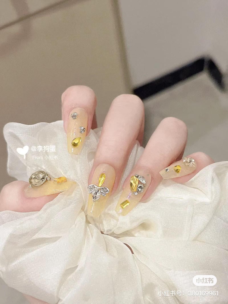 Bàn tay với móng tay trang trí bằng đá quý vàng và bạc, cầm một chiếc khăn vải màu trắng.