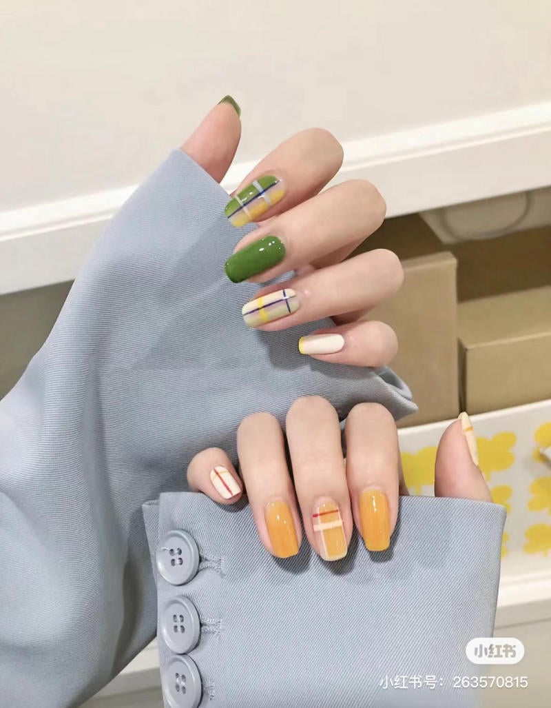 Bàn tay với móng tay được sơn màu xanh, vàng và trắng, có họa tiết kẻ sọc, áo tay dài màu xanh xám.