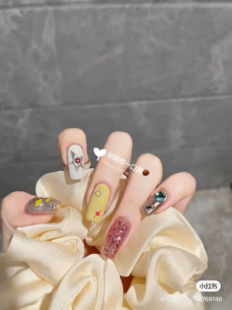 Bàn tay với bộ móng trang trí cầu kỳ, đa dạng màu sắc và họa tiết, cầm một chiếc scrunchie màu kem.