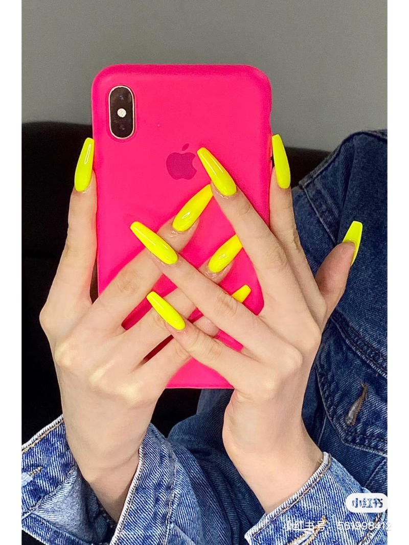 Người cầm điện thoại màu hồng, móng tay dài màu vàng neon nổi bật, mặc áo khoác denim xanh.