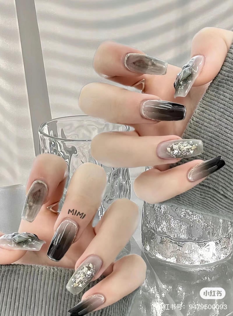 Bàn tay với móng tay được sơn nghệ thuật màu xám và đen, nền là ly thủy tinh và áo len xám.