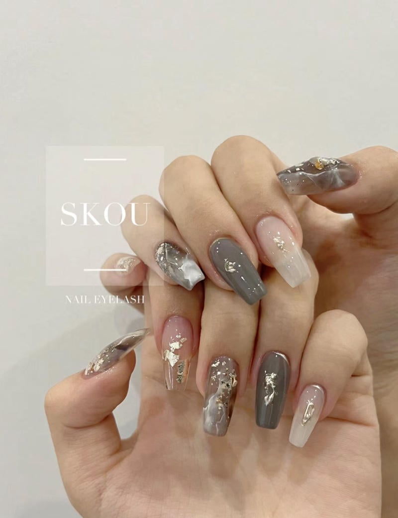 Bàn tay với móng tay dài được sơn màu xám và trắng, trang trí hoa văn ánh kim và họa tiết nhũ.