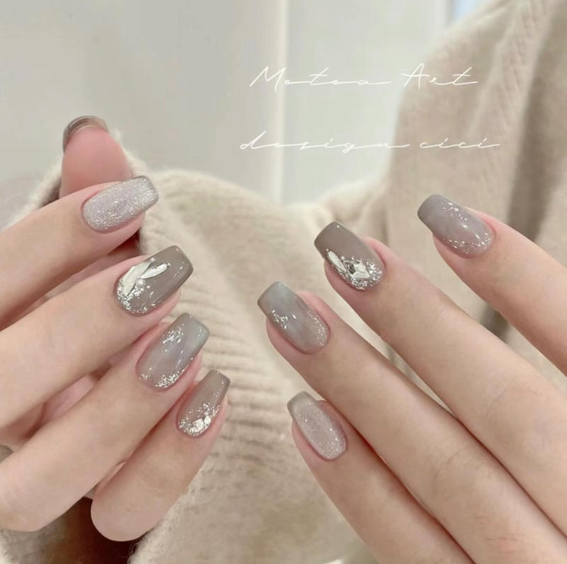 Bàn tay với móng tay được trang trí họa tiết màu xám, bạc, có ánh kim và hoa văn sáng tạo.
