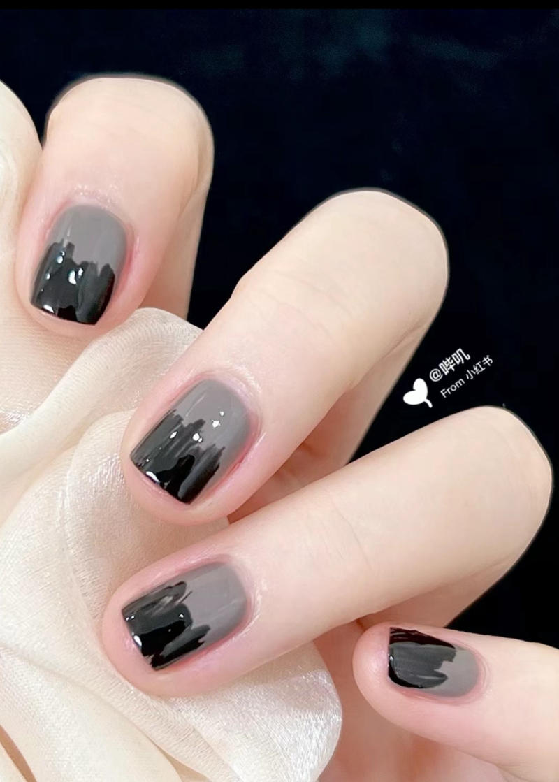 Bàn tay với móng tay được sơn màu đen và xám, cầm một mảnh vải màu trắng.