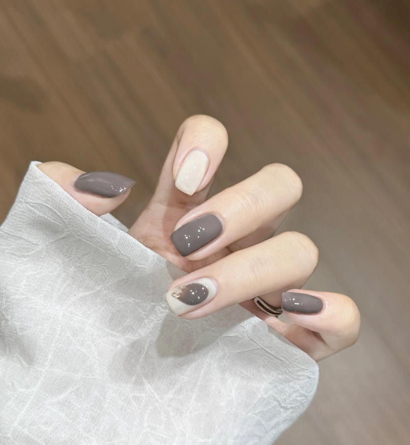 Bàn tay với móng tay sơn màu xám và trắng, họa tiết đơn giản, cầm một tấm vải màu trắng.