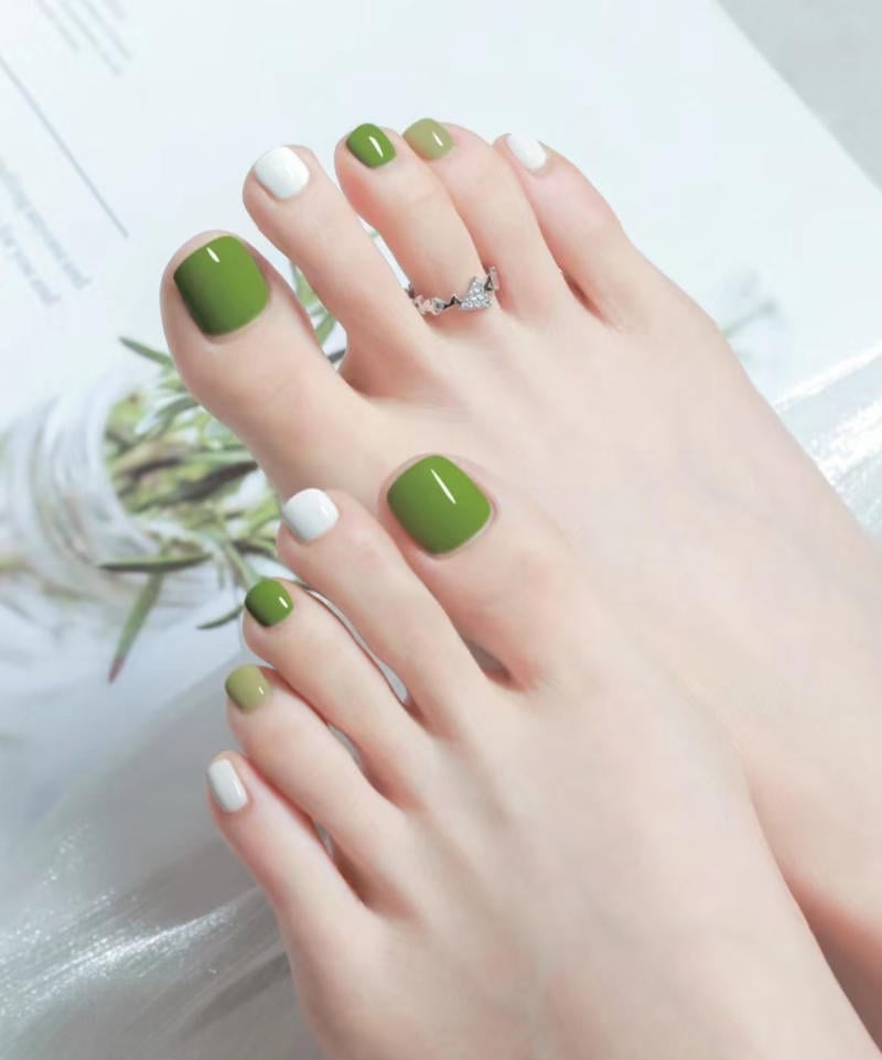 Bàn chân với móng chân sơn màu xanh và trắng, đeo nhẫn bạc, nền trắng mờ.