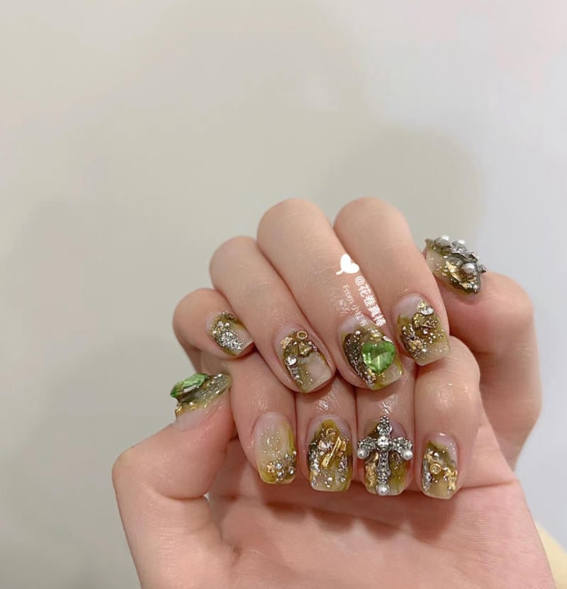 Bàn tay với móng tay được trang trí công phu bằng đá quý và họa tiết lấp lánh, nền màu nhạt.