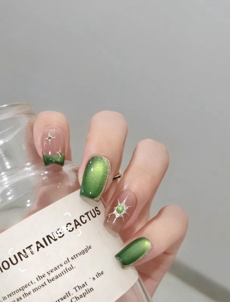 Bàn tay với móng tay sơn màu xanh và họa tiết ngôi sao cầm một chai có chữ trên nhãn.