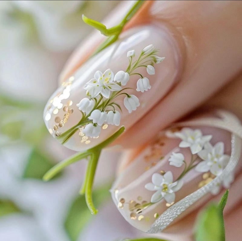 Móng tay trang trí hoa trắng tinh tế và họa tiết ánh kim trên nền sơn trong suốt.
