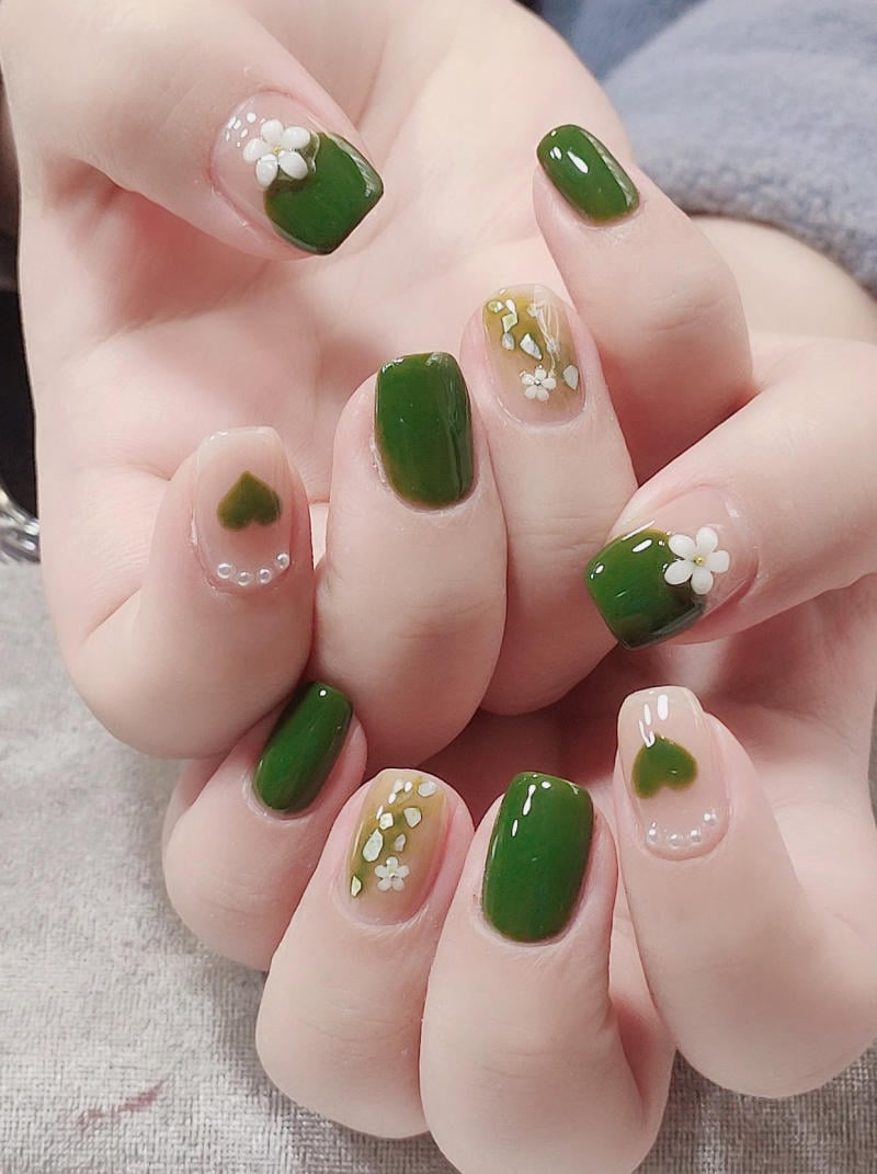 Bàn tay với móng tay được sơn màu xanh lá, trang trí hoa trắng và họa tiết trái tim nhỏ.