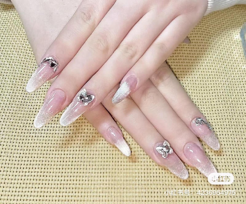 nail-mong-dai__2__a9cd6f261c74424a893d937bbde56331 Bàn tay với móng dài, được trang trí bằng sơn lấp lánh và họa tiết hình nơ.