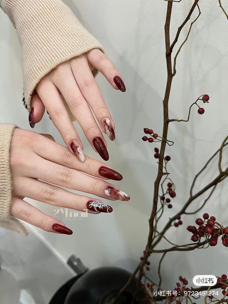 nail-mong-nhon-tron__1__46651f8fcd284e2aa417c9acbcba940e Bàn tay với móng tay sơn đỏ có họa tiết, bên cạnh nhánh cây khô với quả mọng đỏ.