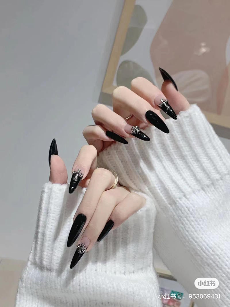 nail-mong-nhon-tron__3__57e88a921e704584878636046225944f Bàn tay với móng tay dài màu đen, đính đá, mặc áo len trắng, nền có bức tranh trừu tượng.