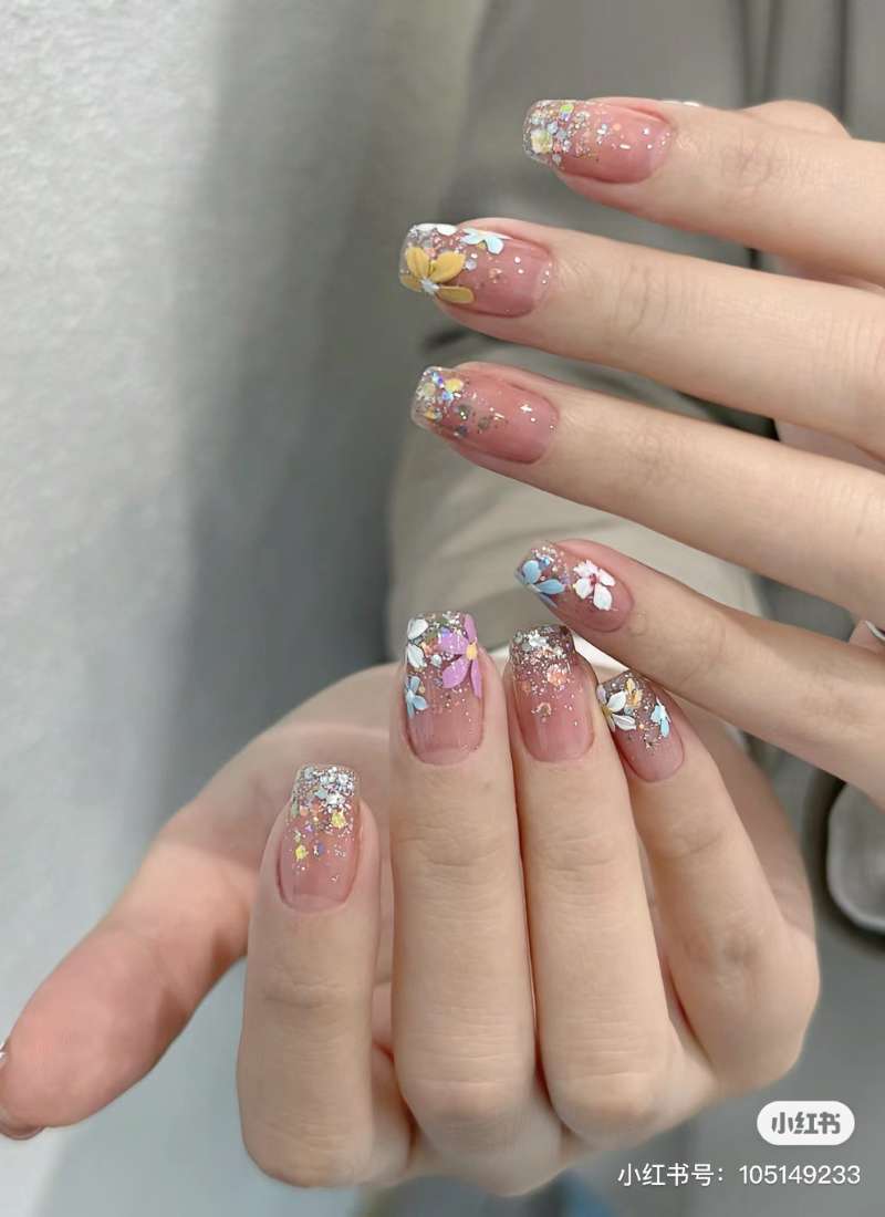 Bàn tay với móng tay được trang trí hoa và kim tuyến lấp lánh, kiểu dáng hiện đại và tinh tế.