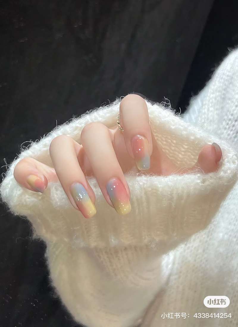 Tay với móng tay sơn màu pastel ombre, mặc áo len trắng, nền tối.