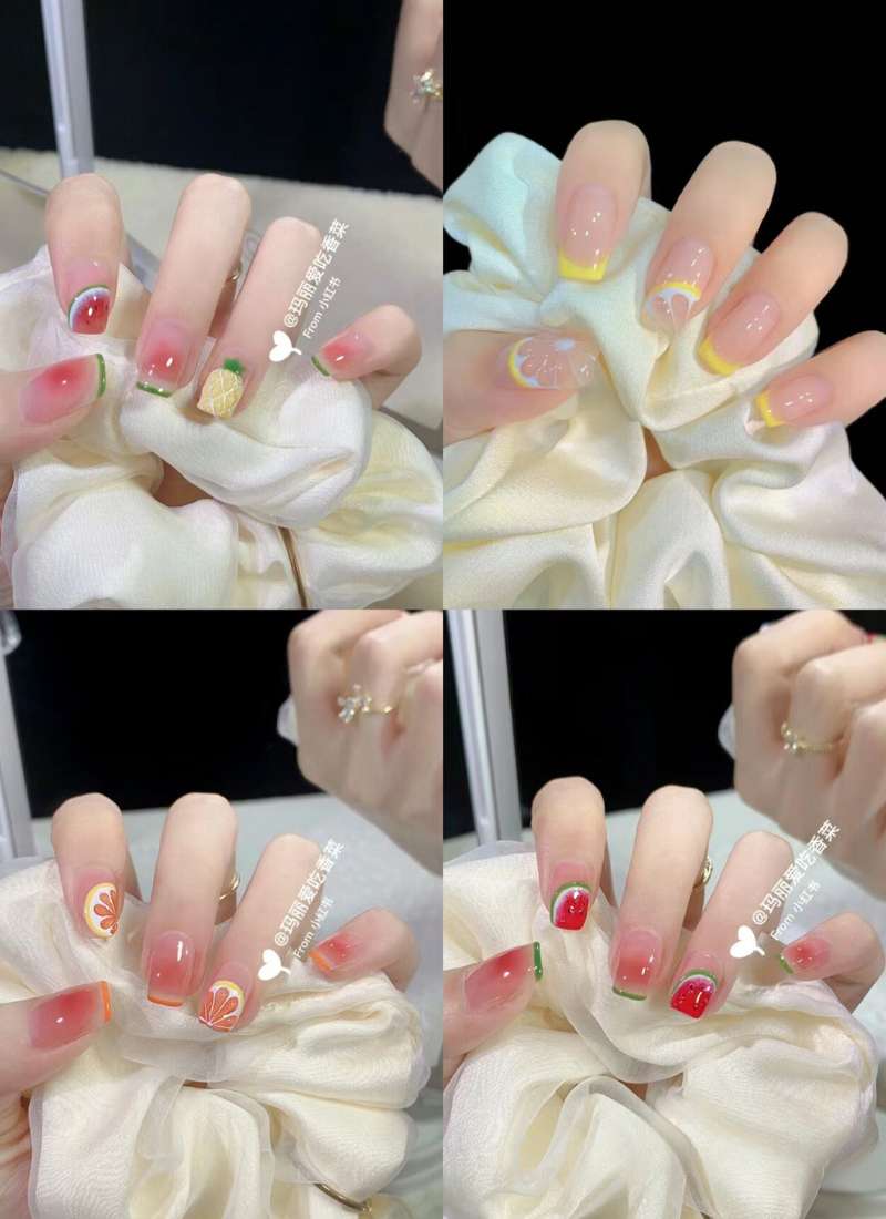 Bộ móng tay với họa tiết trái cây đa dạng, gồm màu đỏ, vàng, cam và xanh, được chụp trên nền vải trắng.