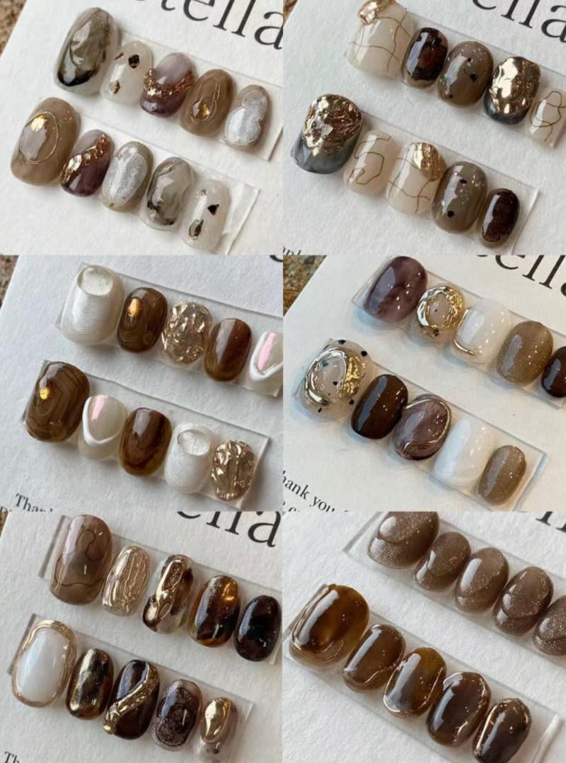 Bộ sưu tập móng tay giả với các thiết kế màu sắc và họa tiết khác nhau trên nền giấy trắng.