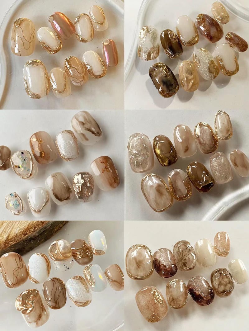 Bộ móng tay giả với nhiều màu sắc tự nhiên, kết hợp các họa tiết ánh kim và vân đá, được sắp xếp trên nền trắng.
