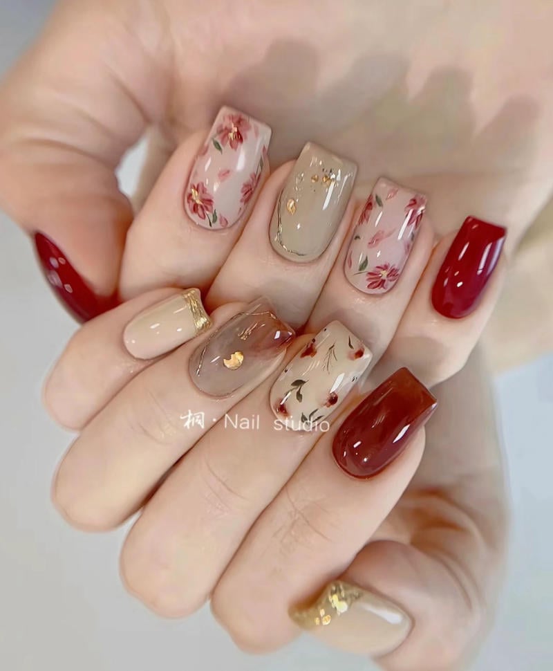 Bàn tay với móng tay được trang trí hoa văn và màu sắc khác nhau, bao gồm đỏ, be và họa tiết hoa.