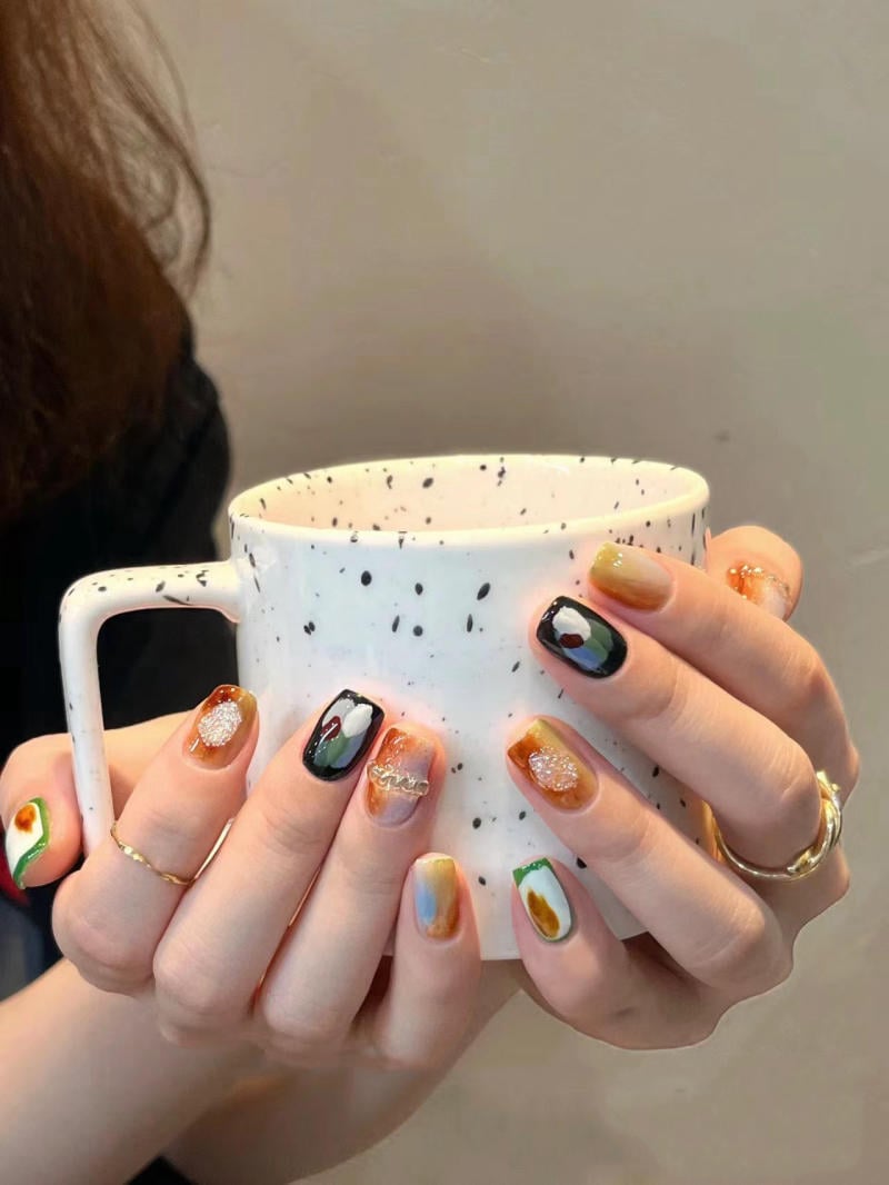 Người cầm cốc trắng có họa tiết đốm đen, móng tay được trang trí nghệ thuật màu sắc đa dạng.