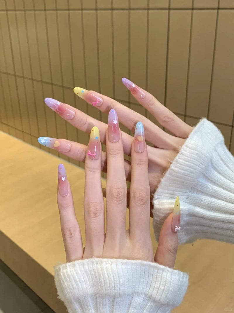 Bàn tay với móng tay dài, được sơn màu pastel và trang trí họa tiết ngôi sao, nổi bật trên nền áo len trắng.