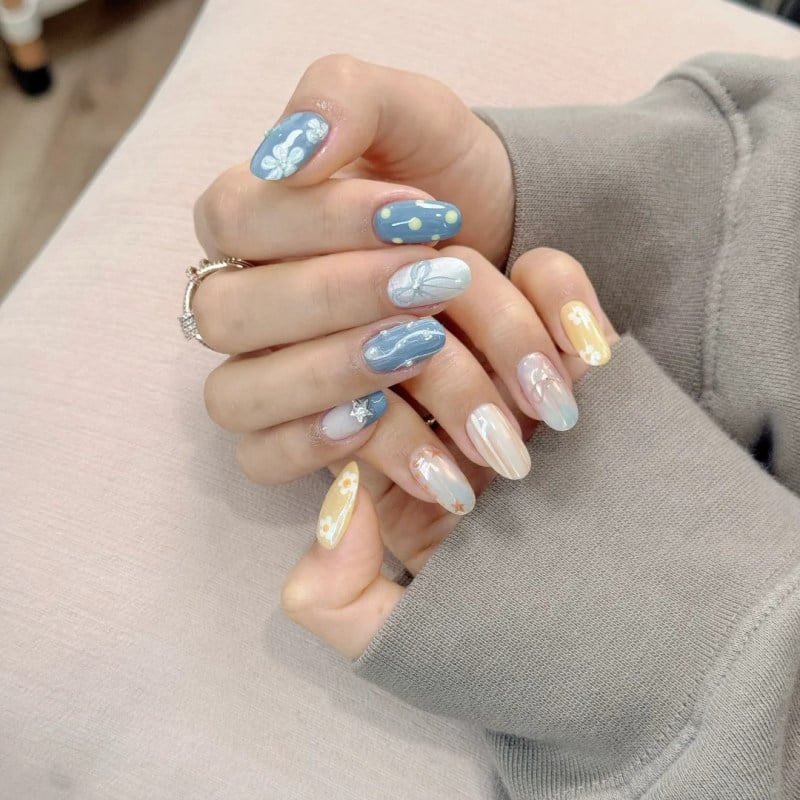 Bàn tay với móng tay được trang trí họa tiết đa dạng và màu sắc pastel, mặc áo tay dài màu xám.