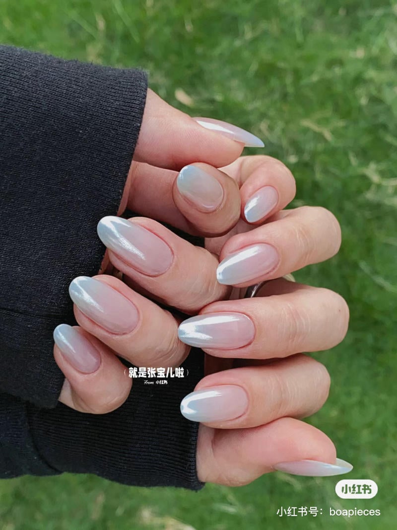 Bàn tay với móng tay sơn màu trắng ngọc trai, nền cỏ xanh.