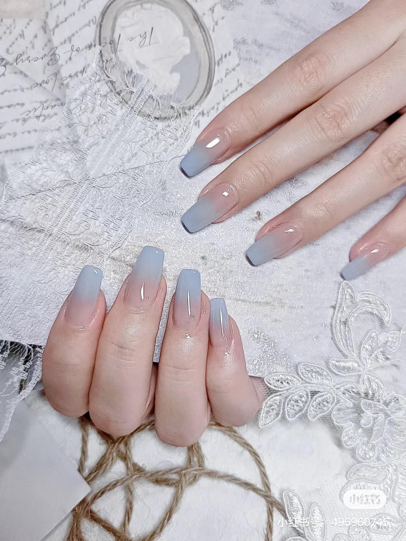 Bàn tay với móng tay sơn màu ombre xanh nhạt, được chụp trên nền vải ren trắng trang trí.