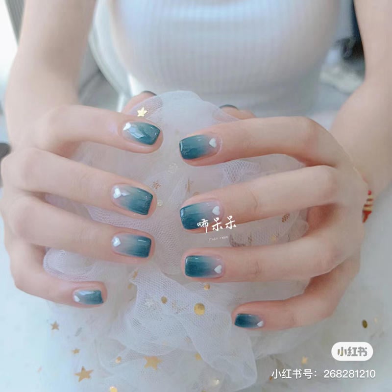 Bàn tay với móng tay sơn màu xanh ombre, đang cầm một chiếc khăn voan trang trí sao vàng.