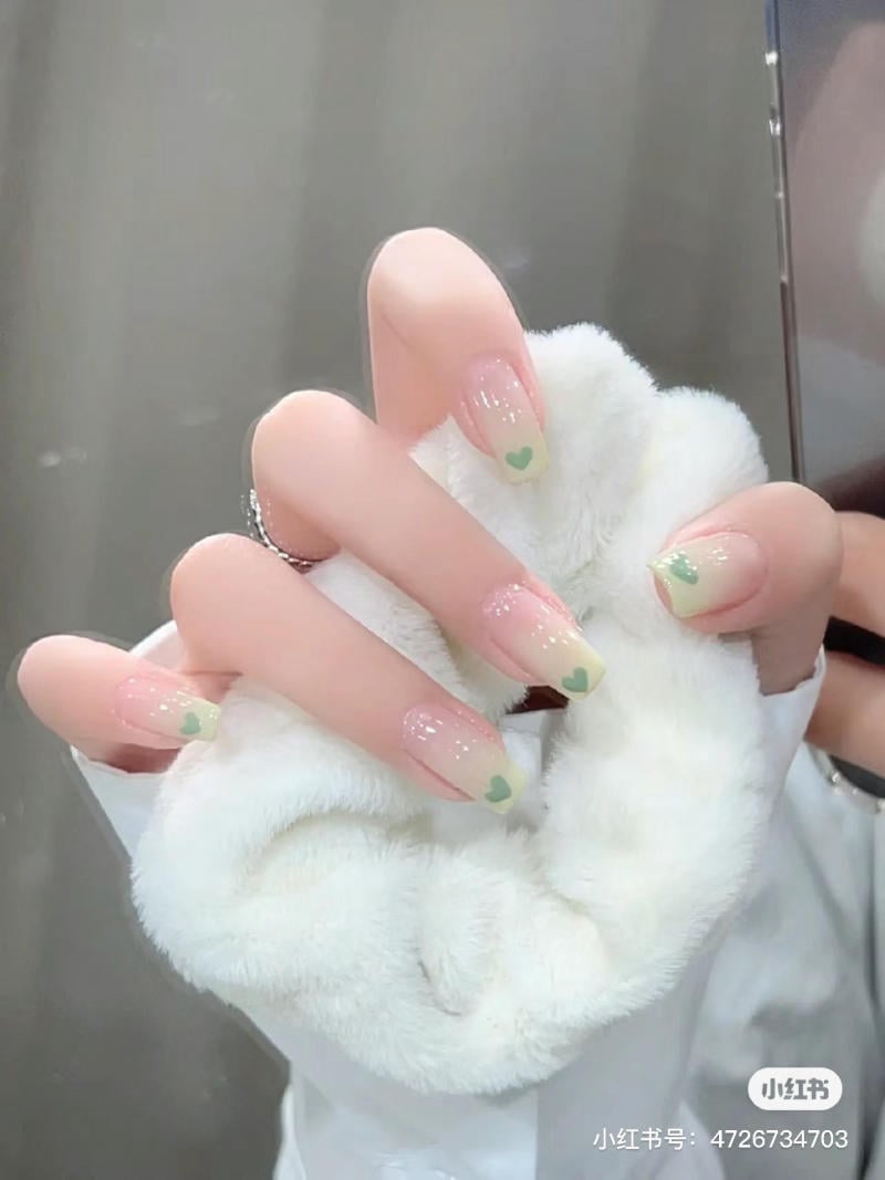 Bàn tay đeo găng lông trắng, móng tay được sơn màu hồng nhạt với họa tiết trái tim xanh.