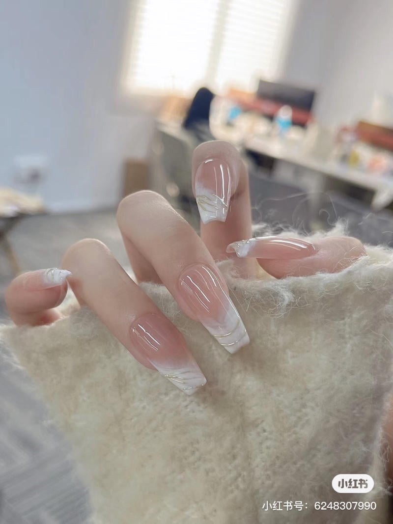 Bàn tay với móng tay dài, sơn màu trong suốt và trắng, được chụp trong phòng có ánh sáng tự nhiên.